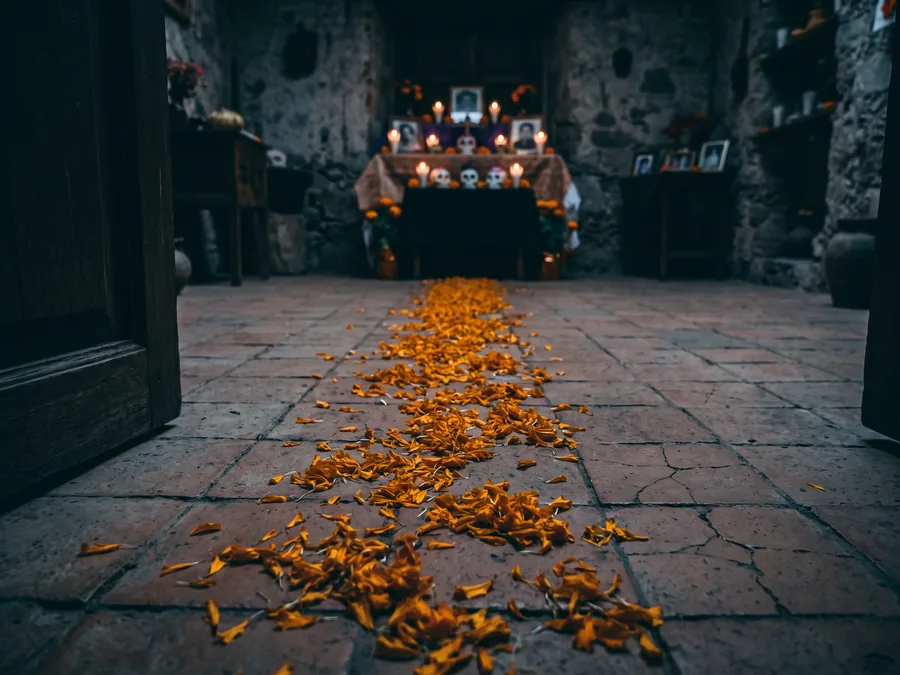 Weg aus orangen Ringelblumenblüten über einen alten Steinboden, der von einer Tür zu einem kerzenbeleuchteten Altar führt