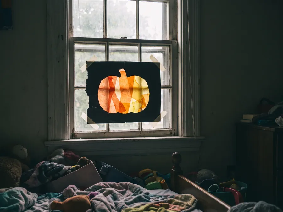 Fensterbild aus schwarzem Karton mit ausgeschnittenem Kürbis, von hinten mit orangem Transparentpapier beklebt, im Gegenlicht