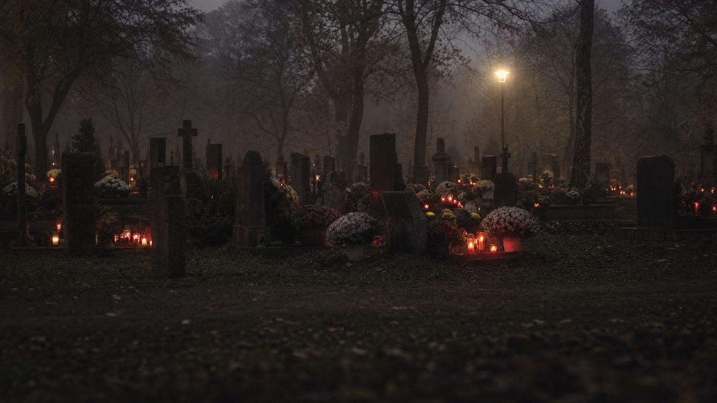 Friedhof in der Dämmerung mit vielen roten Grablichtern zwischen Chrysanthemen
