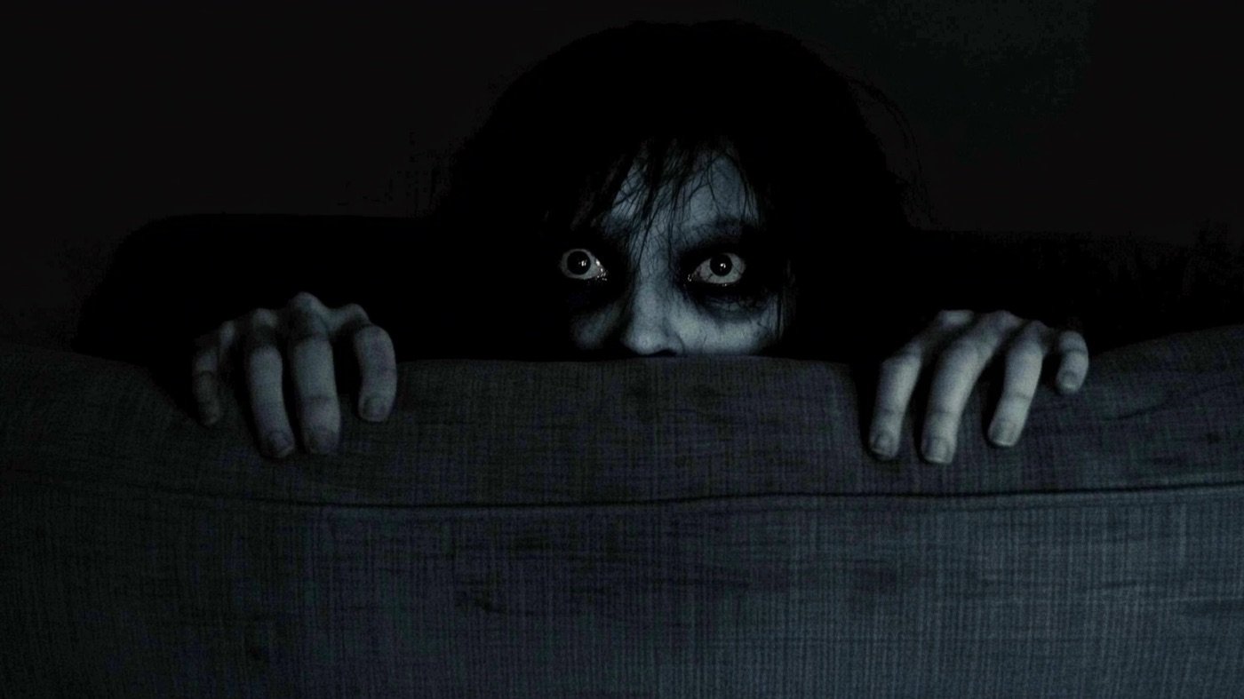 Erschreckende Gestalt hinter einer Sofalehne beim Horrorfilm-Abend im dunklen Wohnzimmer
