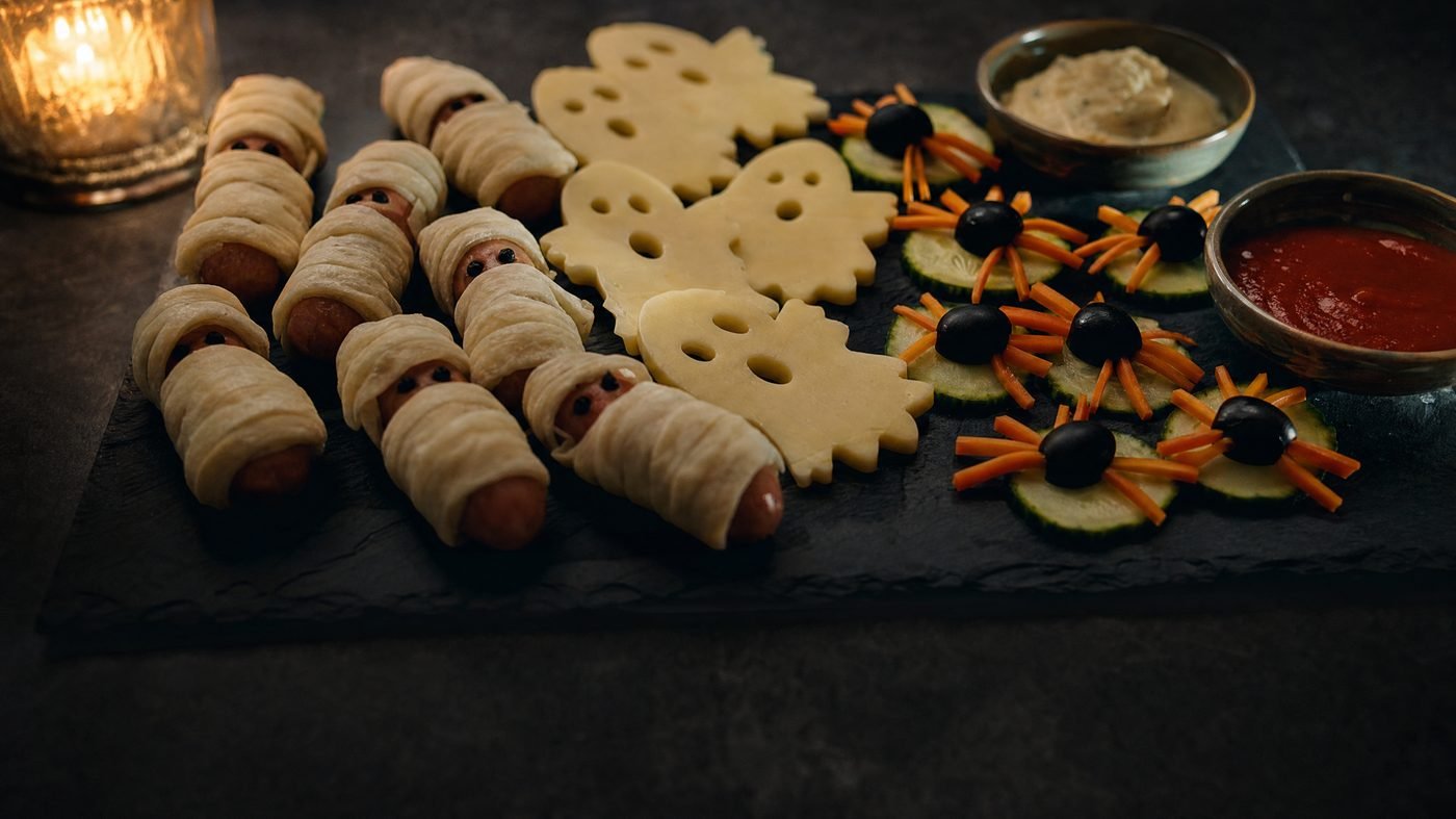 Schieferplatte mit Halloween-Fingerfood: Mumien-Würstchen, Käse-Gespenster und Gemüsespinnen
