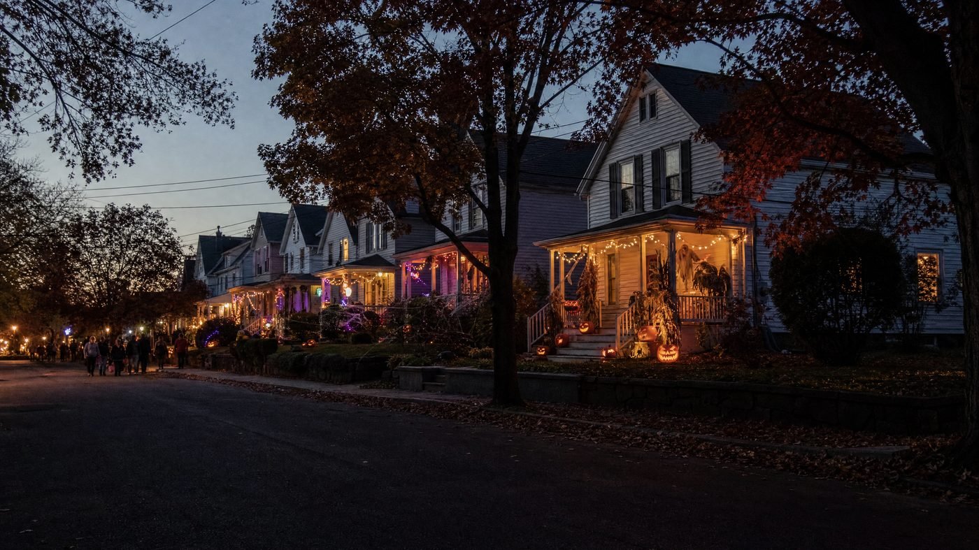 Amerikanische Vorstadtstraße am Halloween-Abend mit geschmückten, beleuchteten Veranden und Kürbissen