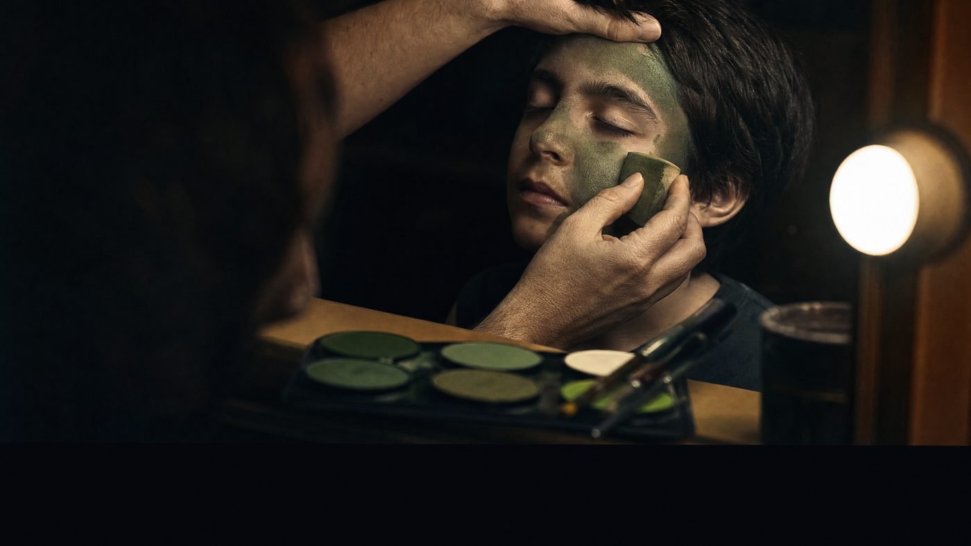Hände tragen mit einem Schwämmchen grüne Schminke auf, daneben Palette und Pinsel
