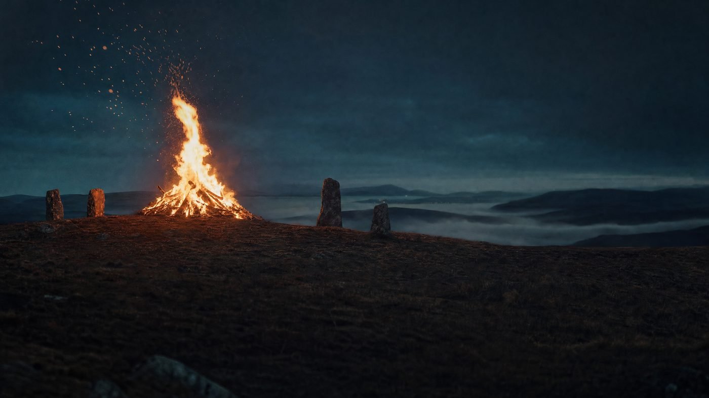 Großes Samhain-Feuer auf einem irischen Hügel bei Nacht, daneben stehende Steine im Nebel