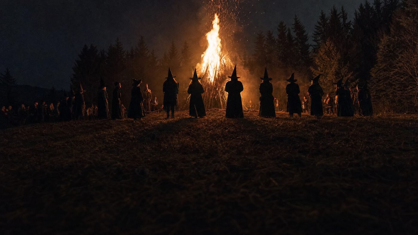 Walpurgisfeuer bei Nacht, als Hexen verkleidete Menschen stehen als Silhouetten um die Flammen