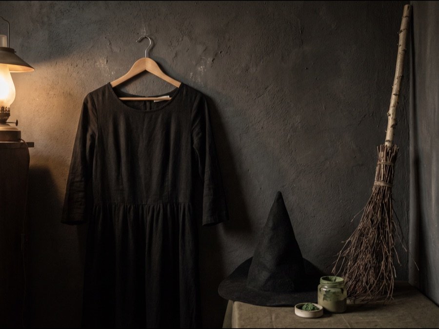 Schwarzes Kleid mit spitzem Hut, daneben grüne Schminke und ein Besen aus Reisig