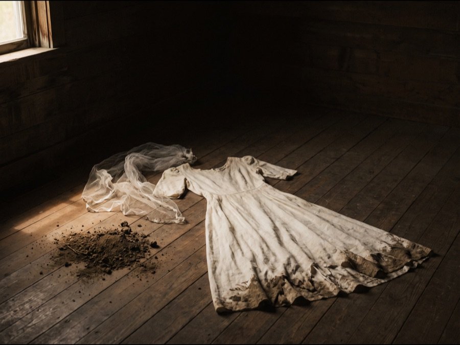 Weißes Kleid mit eingerissenem Saum, daneben Erde und ein Stück Schleierstoff