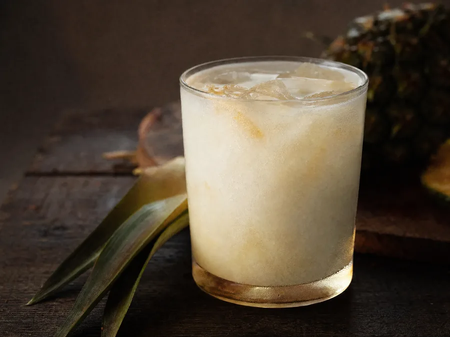 Milchig-weißer Cocktail aus Kokosmilch und Ananassaft auf Eis