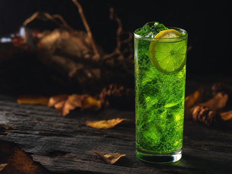 Giftgrüner Longdrink mit Eis und Zitronenscheibe