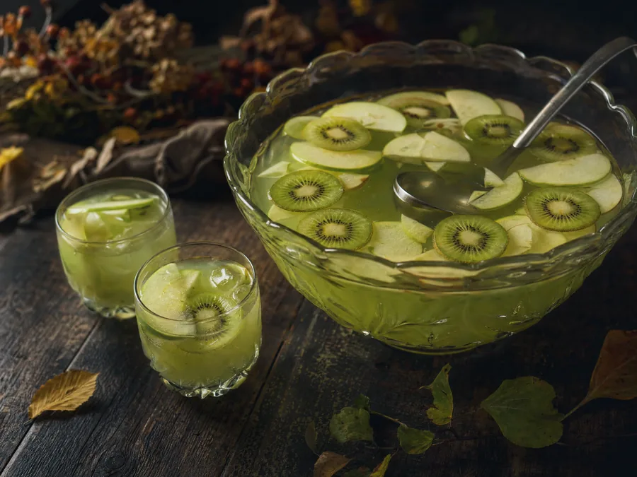 Trüb-grüner Hexentrank in einer großen Bowleschüssel mit Kiwi- und Apfelscheiben