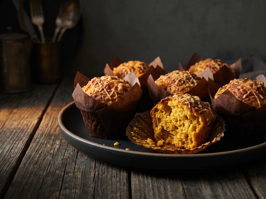 Herzhafte Kürbis-Muffins mit geriebenem Käse, einer davon aufgebrochen