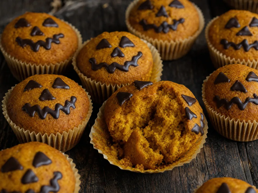 Kürbis-Muffins mit aufgemalten Jack-o'-Lantern-Gesichtern aus dunkler Kuvertüre