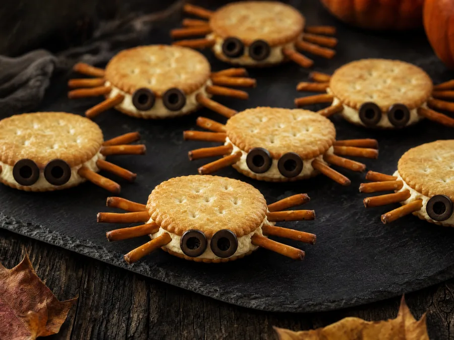 Cracker mit Frischkäse und Salzstangen als Spinnenbeine, Oliven als Augen