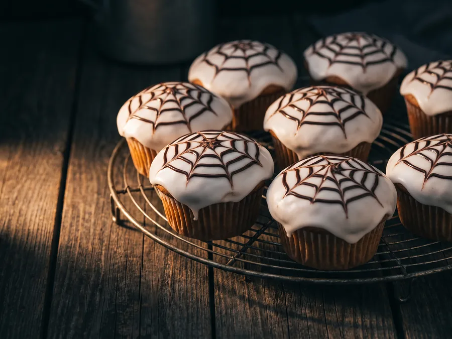 Muffins mit weißem Zuckerguss und aufgezogenem Spinnennetz aus Schokolade