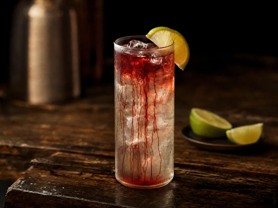 Cocktail mit roten Grenadine-Schlieren, die vom Glasrand nach unten ziehen