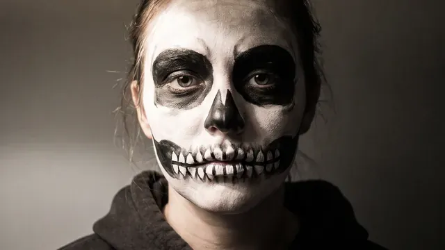 Als Totenkopf geschminktes Gesicht mit großen schwarzen Augenhöhlen und einer über beide Lippen gemalten Zahnreihe