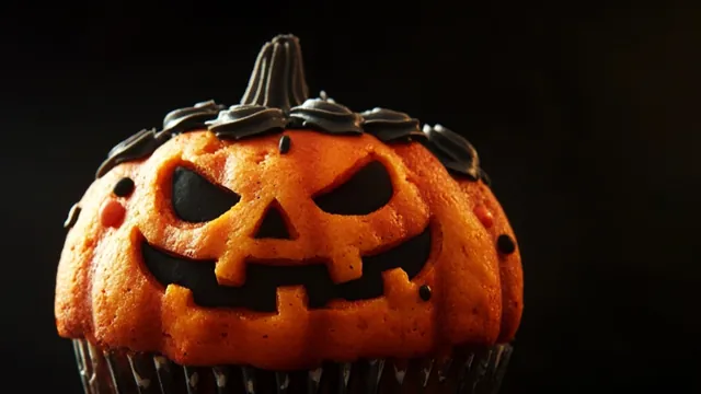 Halloween-Muffin in Kürbisform mit einem Jack-o'-Lantern-Gesicht aus dunkler Schokolade